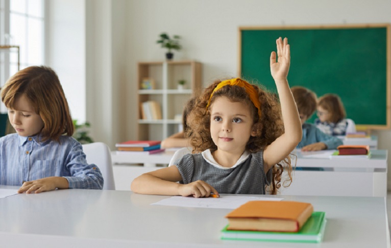 Elementary school student raises her hand, ready to answer the teacher’s questions in class.