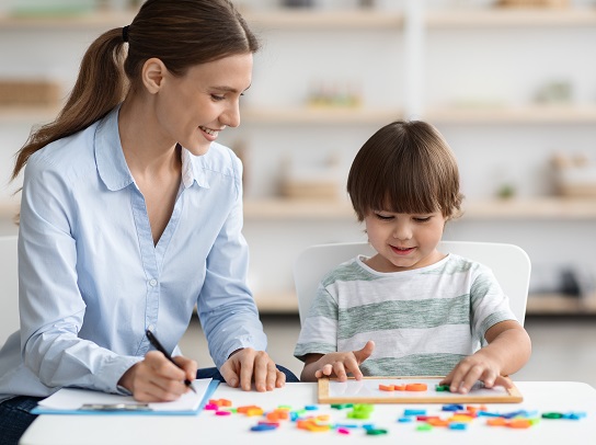 Professional woman language teacher exercising with preschooler, little boy making word with letters, free space