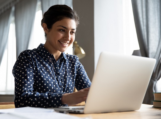 Smiling indian girl student professional typing on laptop at table