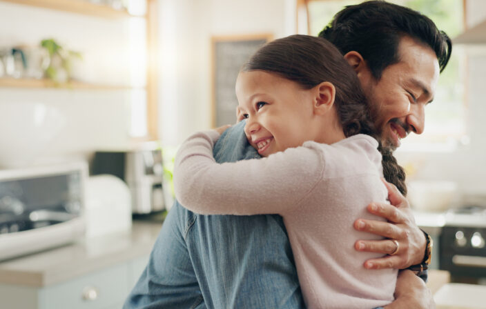 Family, father and daughter hug in the kitchen for love, trust or bonding together in their home. Kids, smile and safety with a happy young man embracing his adorable girl child in their house