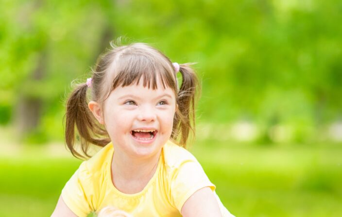 Portrait of a joyful little girl with syndrome down in a summer