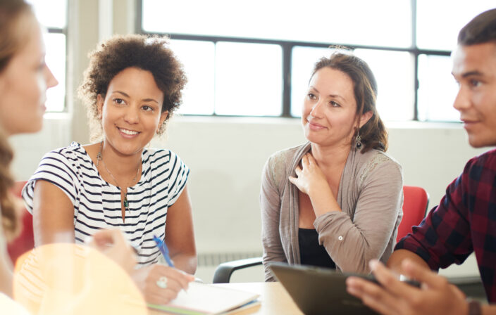 Unposed group of creative business entrepreneurs in an open concept office brainstorming together on a digital tablet.